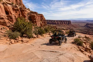 Two UTVs driving along a scenic red rock trail in Utah surrounded by canyon cliffs and desert landscapes